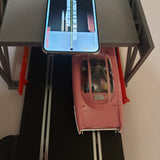Phone displaying a video of a red toy car on a black platform with a gray stand.